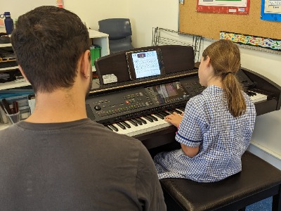 Student playing keyboard with teacher guidance during music lesson