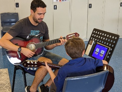 Teacher and student practising guitar together during one-on-one music lesson