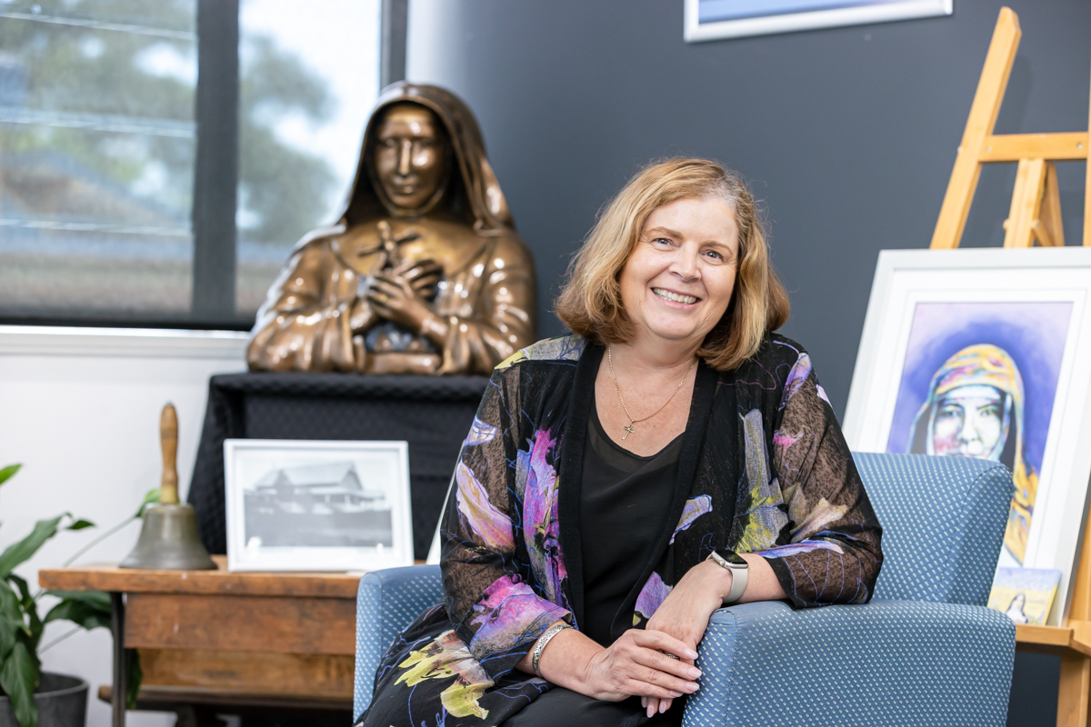 Mrs. Sally Smith Principal seated in school setting with religious statue, artwork and historical displays in background