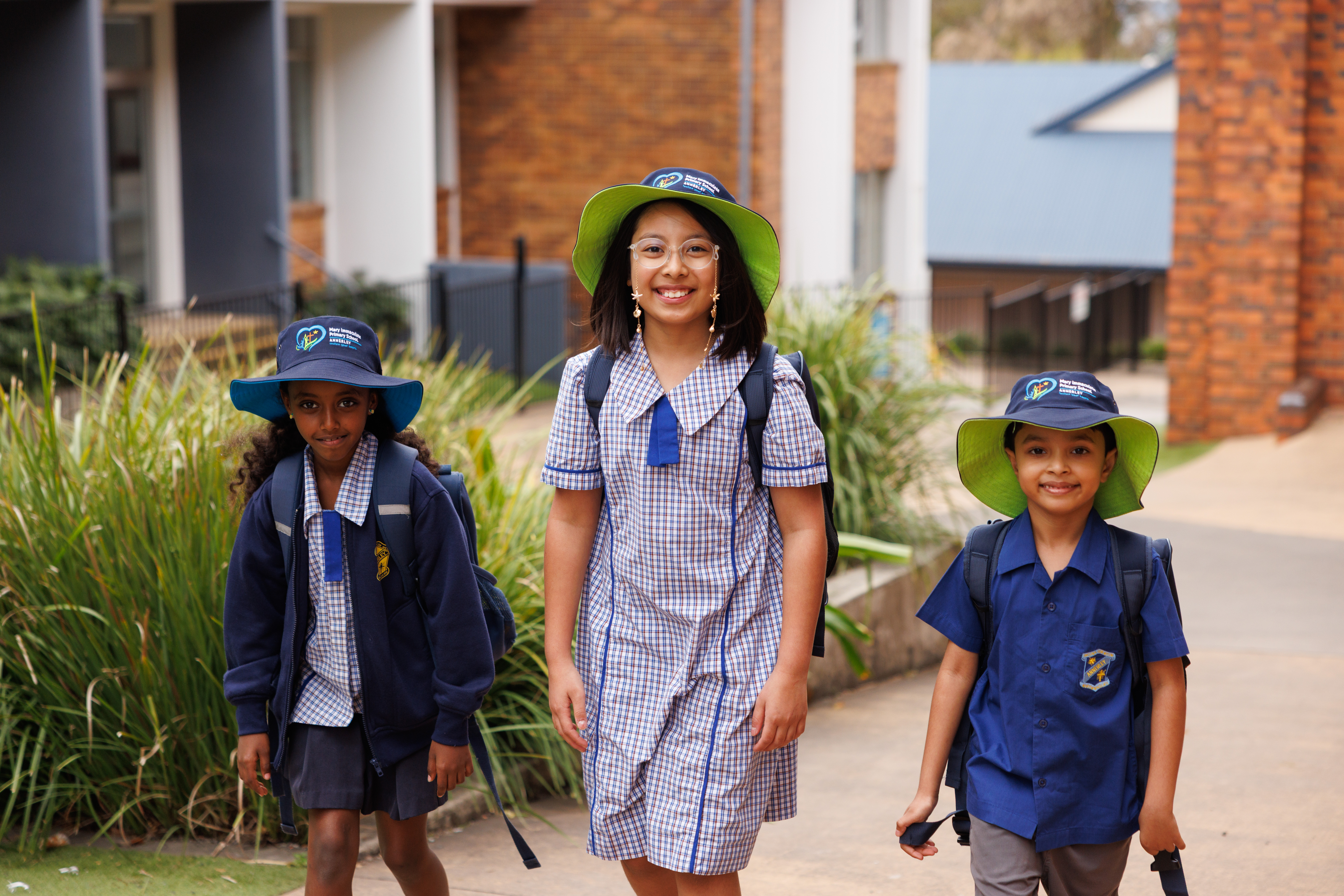 Students wearing school uniforms and hats walking together on pathway outside brick school building